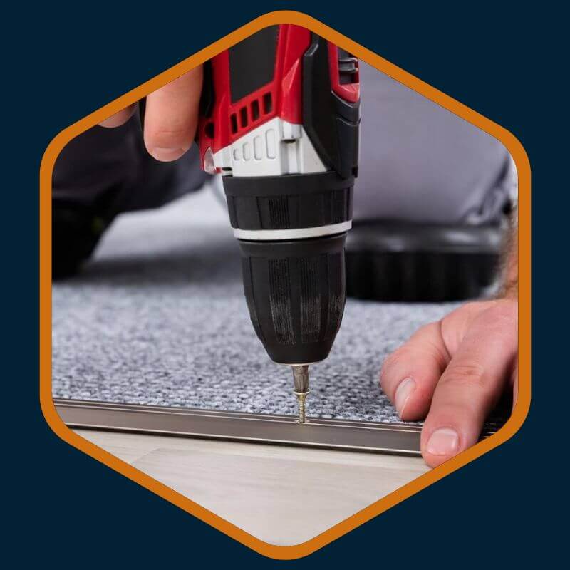Technician's hand drilling a screw into a fitted carpet during repairs by Kairos Upholstery in Bryanston.