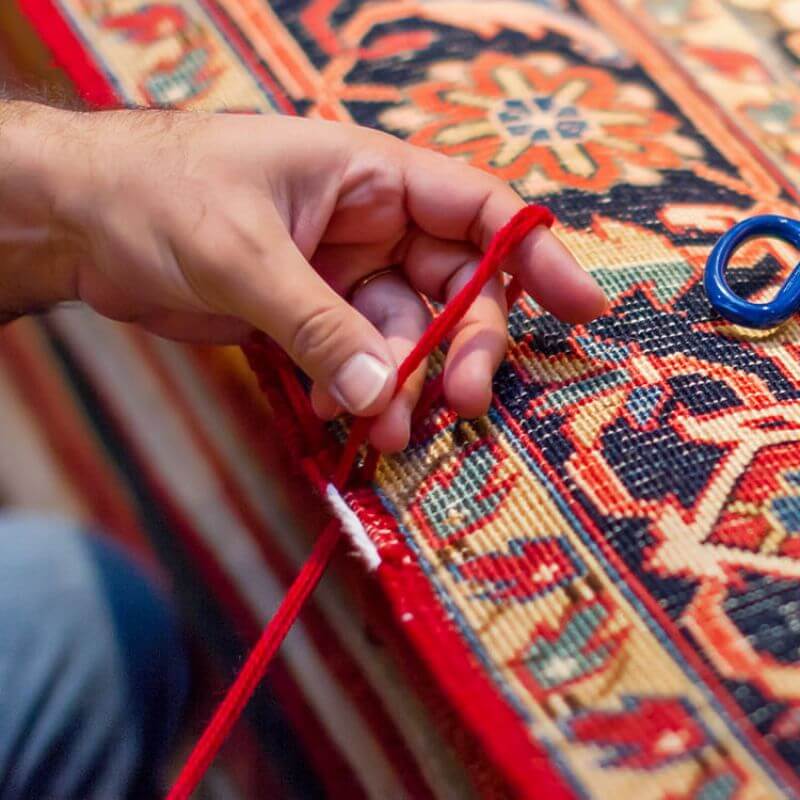 A hand of a technician repairing a Persian rug, showcasing Kairos Upholstery's expert rugs repairing services in Pretoria.